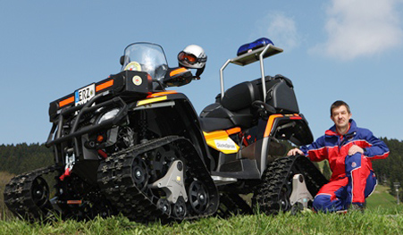 Ein Mitarbeiter der Bergwacht neben einem Quad Motorrad mit Ketten statt Rädern.